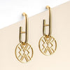 Gold earrings with geometric designs on a beige background
